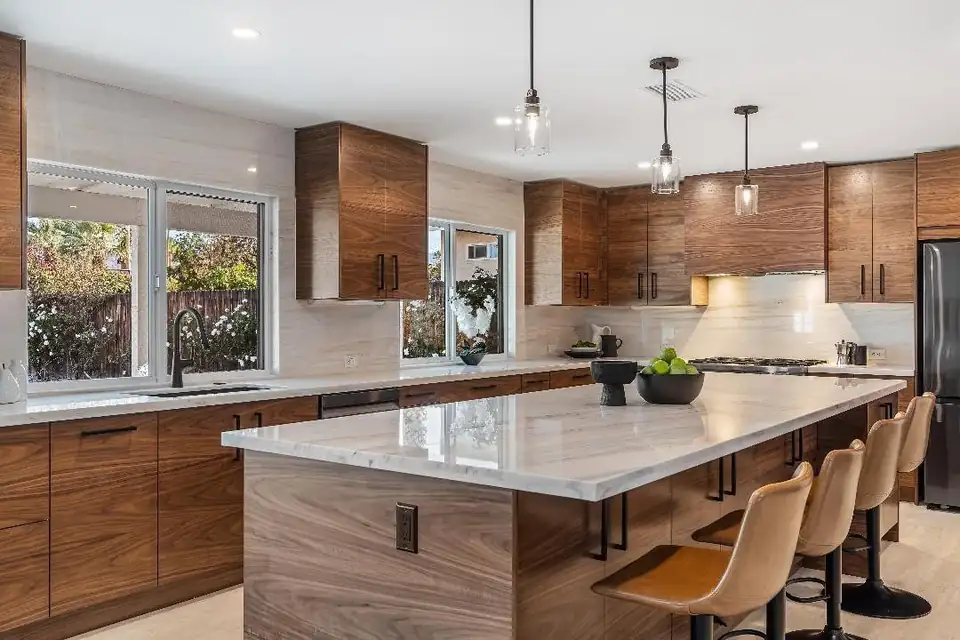 Walnut slab-front kitchen with a long marble-look island, pendant lights and tan leather stools, from INNOVATION Cabinetry Installs, an IKEA cabinet installation specialist serving Palm Springs to Los Angeles