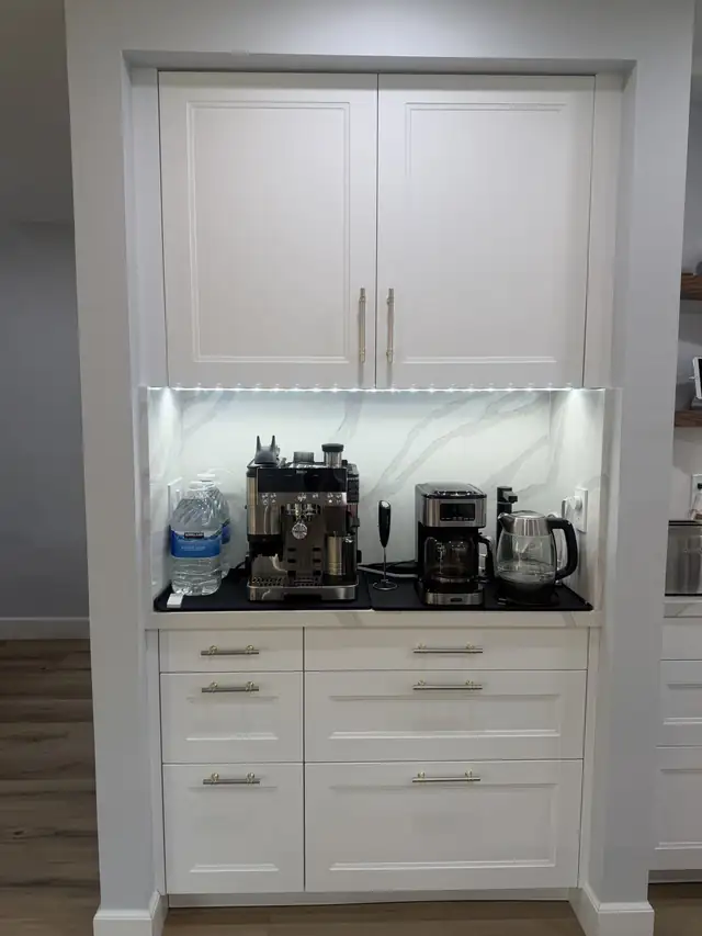 White cabinet coffee station with marble-look backsplash, black counter and under-cabinet lighting