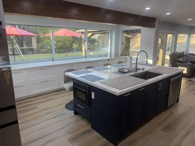 Navy blue island with undermount sink and white quartz top in front of a large picture window