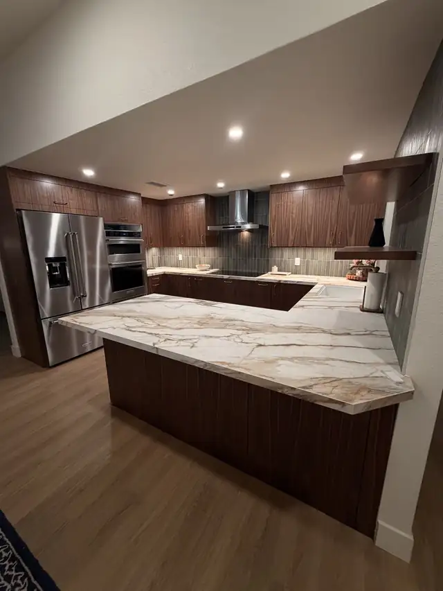 Walnut kitchen with an L-shaped marble-look island, stainless French-door refrigerator and wall ovens