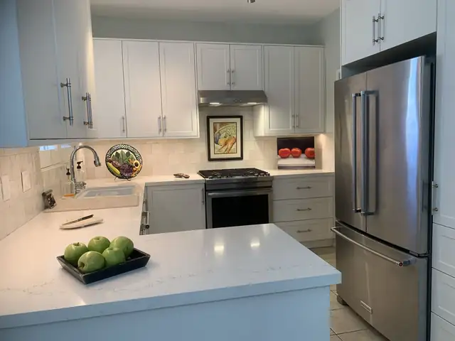White kitchen with a white quartz-style peninsula, stainless refrigerator and white shaker cabinets